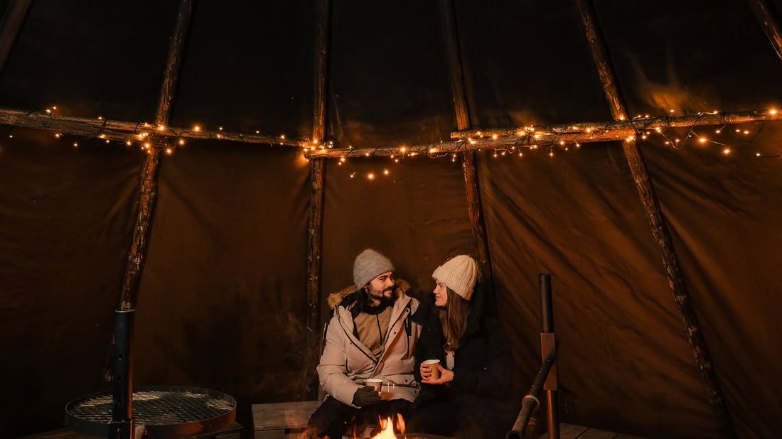 Gäste am Feuer in einer beleuchteten Kota-Hütte