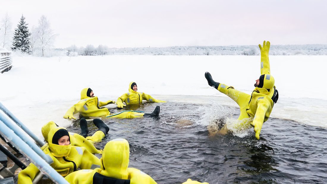Visitantes flotando en un agujero en el hielo con trajes de supervivencia amarillos