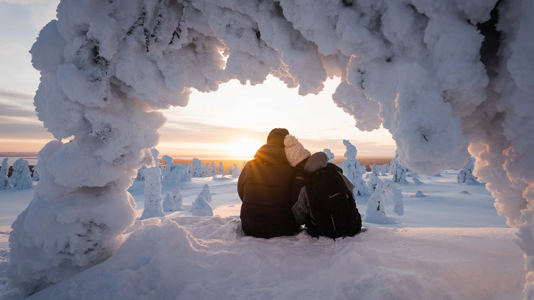 Two guests under a snow arch at sunset