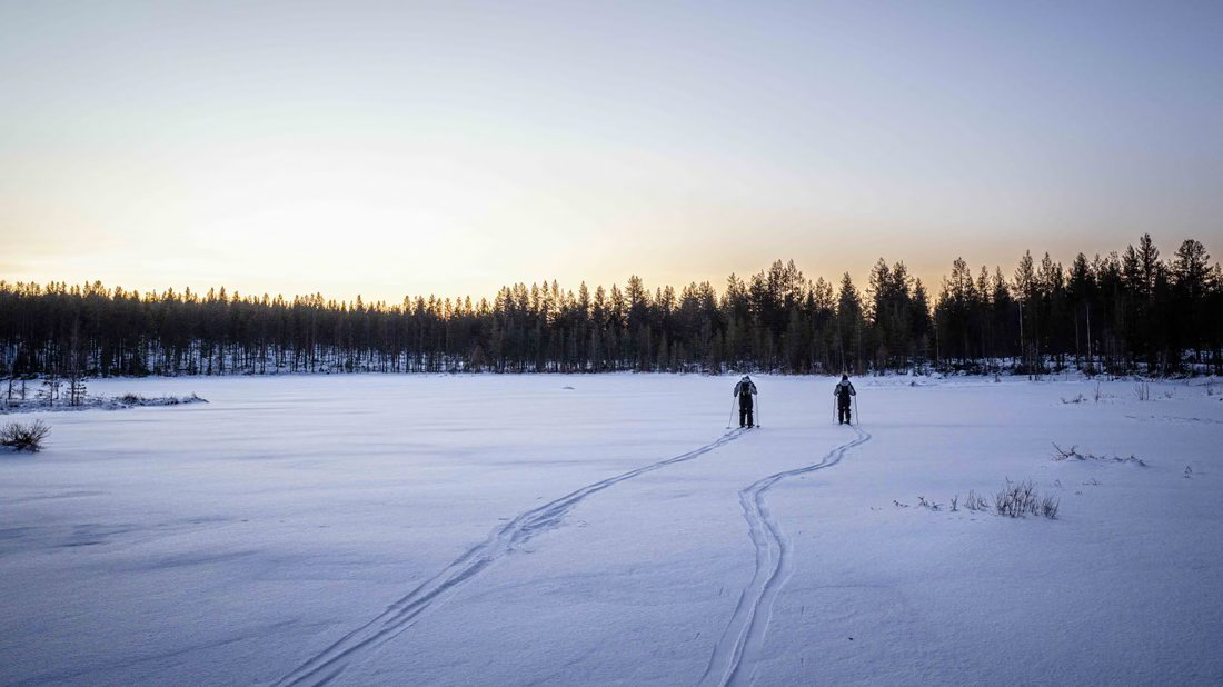Skifahrer überqueren bei Sonnenuntergang einen zugefrorenen See