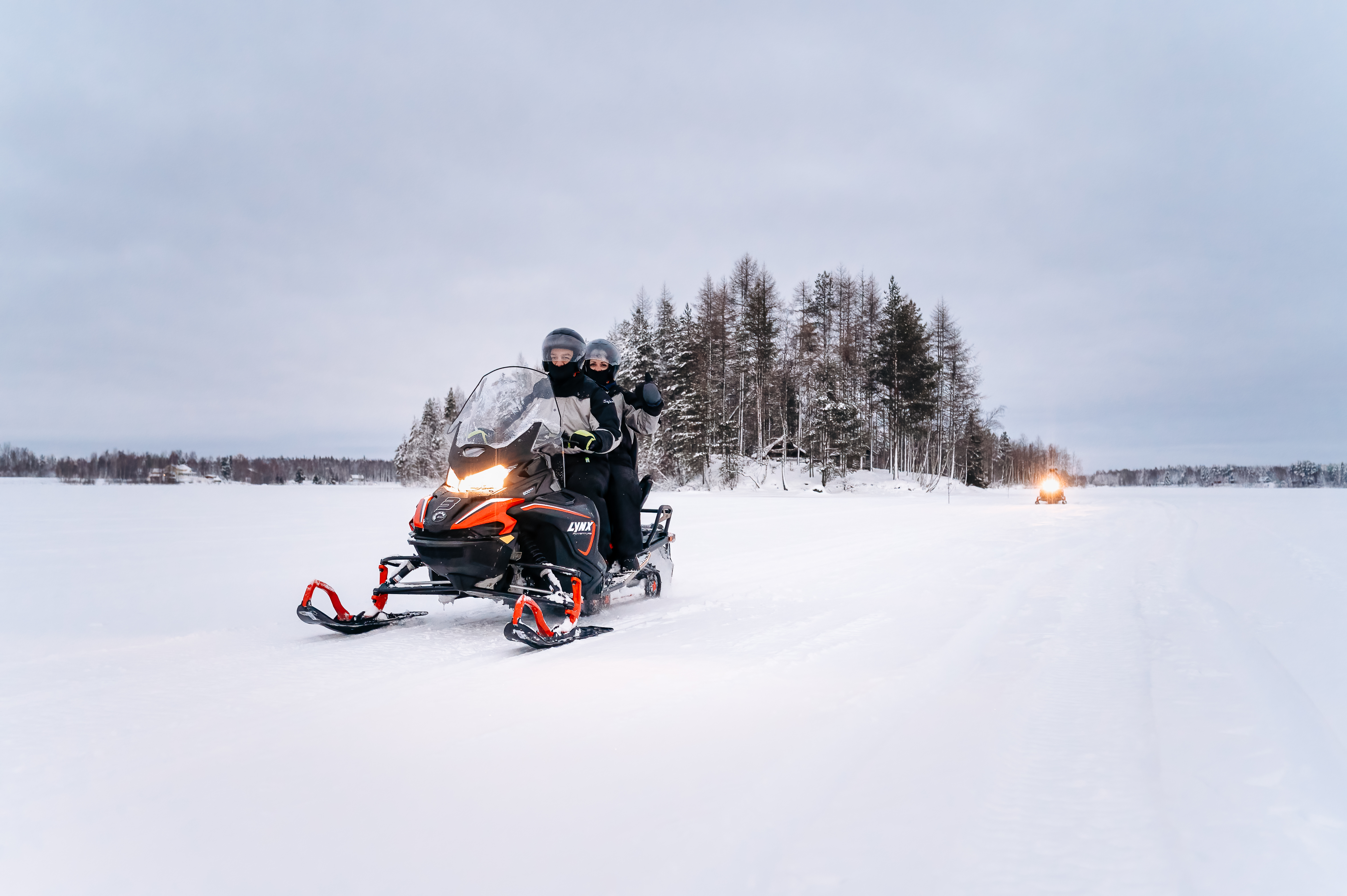 Zwei Gäste fahren mit einem Schneemobil über einen zugefrorenen See
